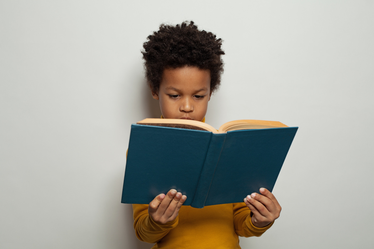 Serious black kid boy reading a book on white background